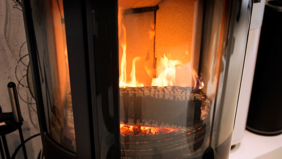 Ett vedträ brinner med ljusa lågor i en braskamin med glasfönster. Foto: Johan Pontén