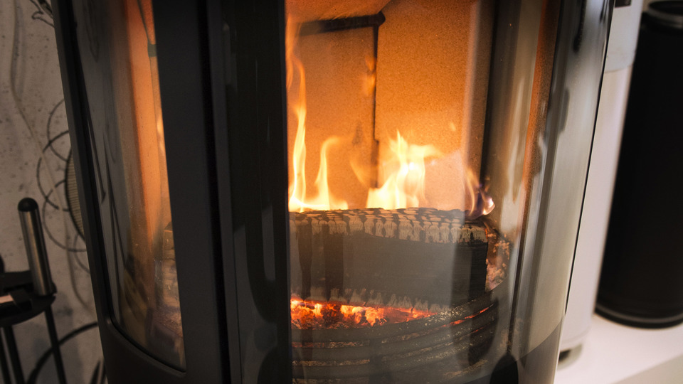 Ett vedträ brinner med ljusa lågor i en braskamin med glasfönster. Foto: Johan Pontén