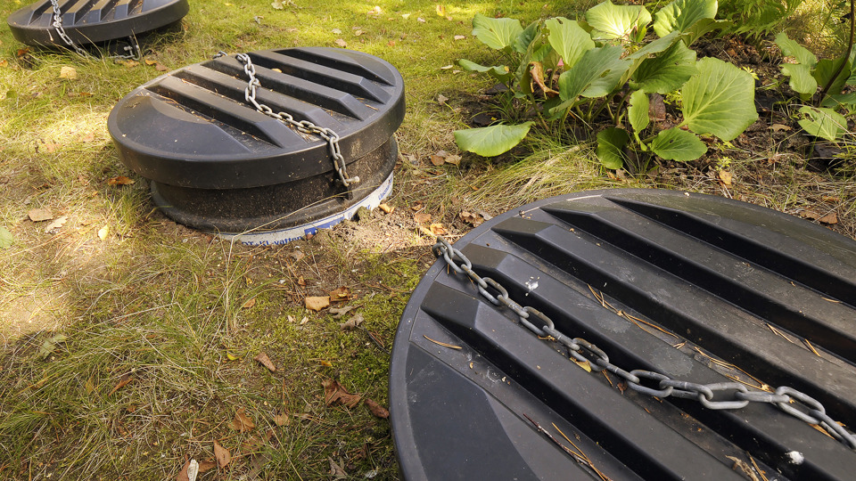 Tre stora svarta plastlock till en trekammarbrunn löper diagonalt över bilden. Foto: Johan Pontén