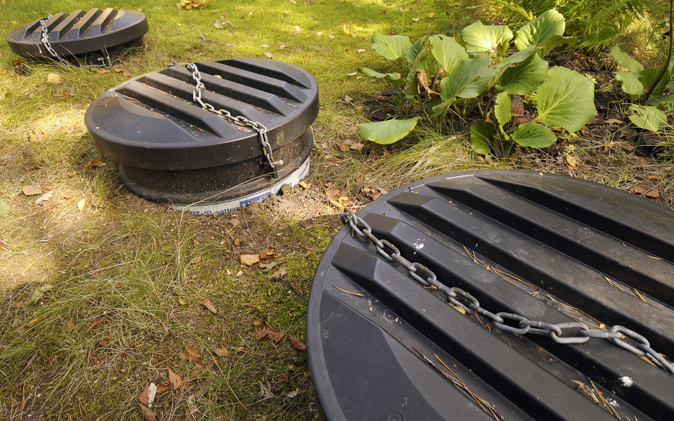 Tre stora svarta plastlock till en trekammarbrunn löper diagonalt över bilden. Foto: Johan Pontén